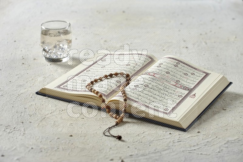 Quran with dates, prayer beads and different drinks all placed on textured white background