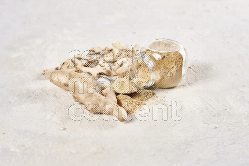 A glass jar full of ground ginger powder flipped with some spilling powder on white background