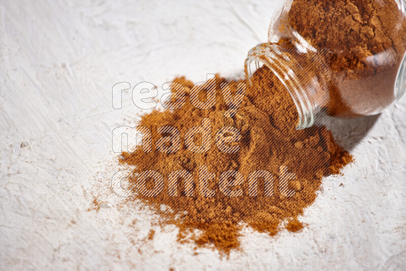 A glass jar full of ground paprika powder flipped with some spilling powder on white background