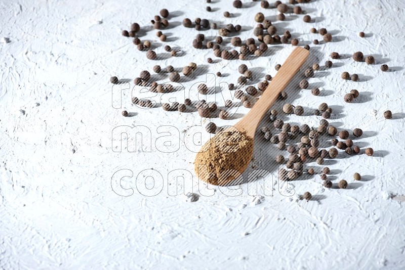 Wooden spoons full of allspice powder and allspice whole balls spreaded on a textured white flooring