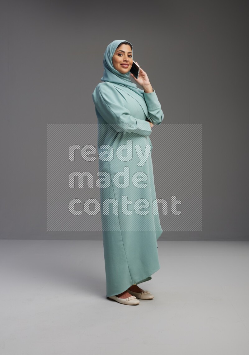 Saudi Woman wearing Abaya standing talking on phone on Gray background