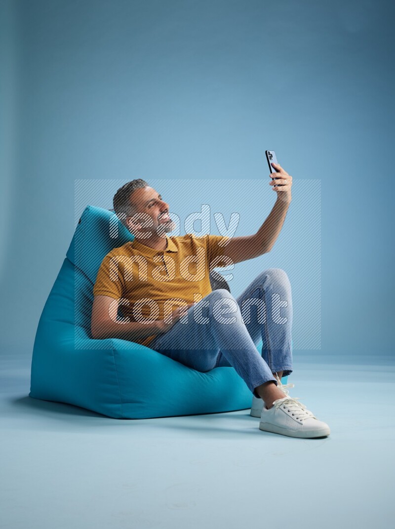 A man sitting on a blue beanbag and taking selfie