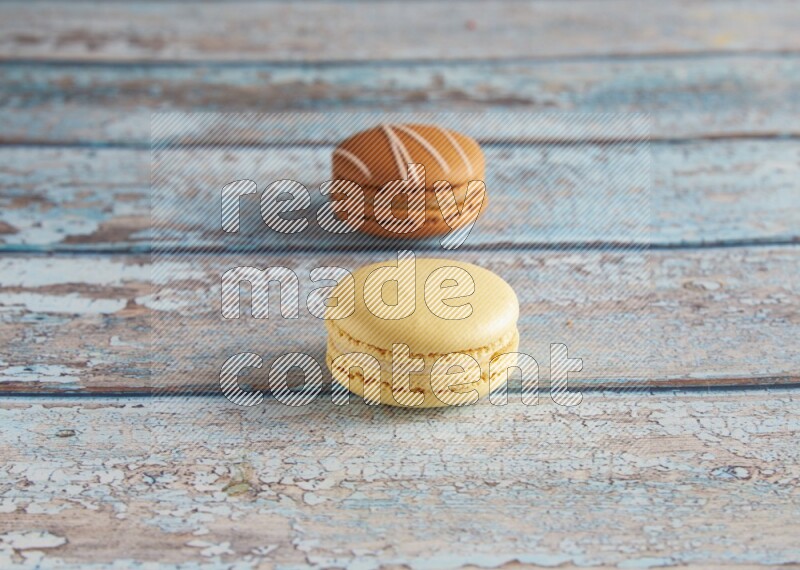 45º Shot of of two assorted Brown Irish Cream, and Yellow Vanilla macarons on light blue background