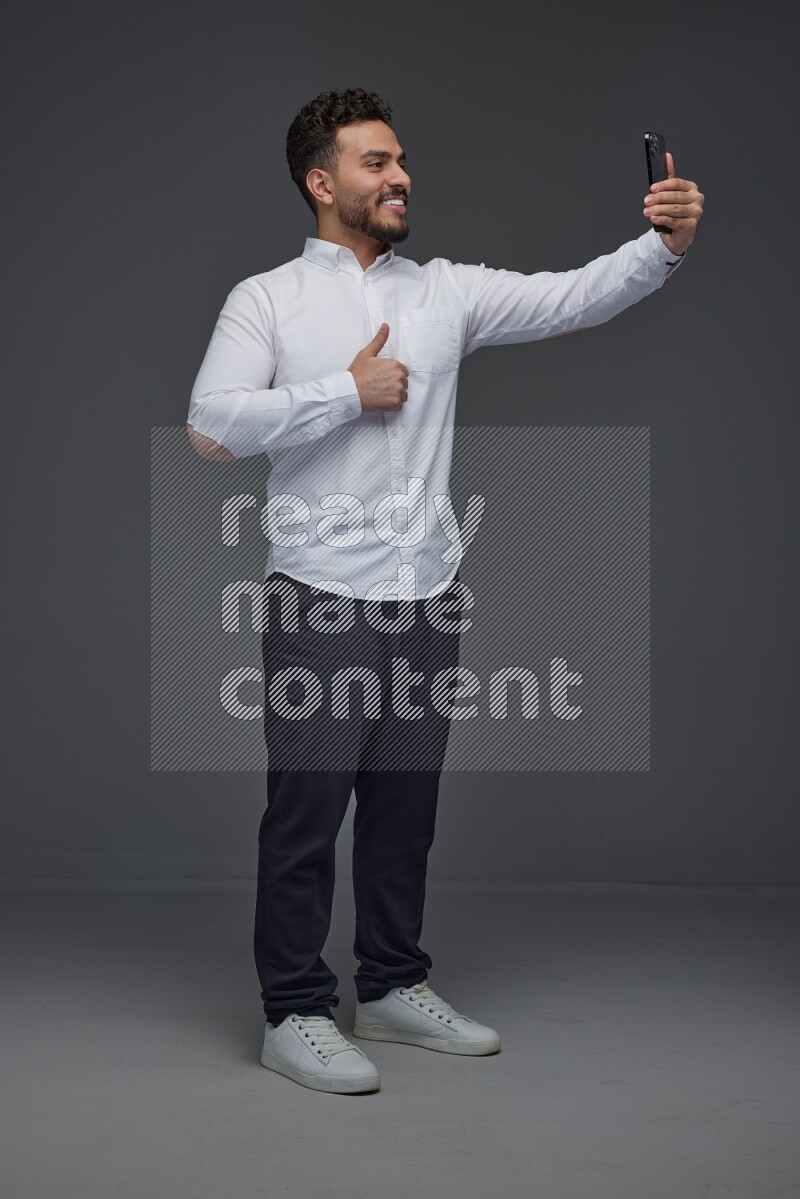 A man wearing smart casual and taking selfie with his phone eye level on a gray background
