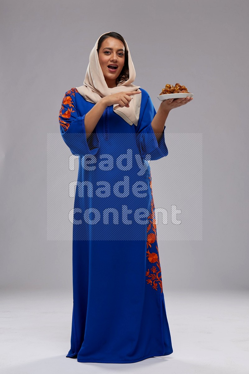 A Saudi woman standing wearing Jalabeya holding a plate of dates