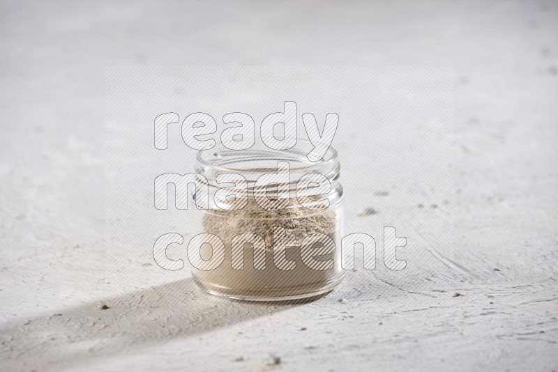 A glass jar full of garlic powder on a textured white flooring in different angles