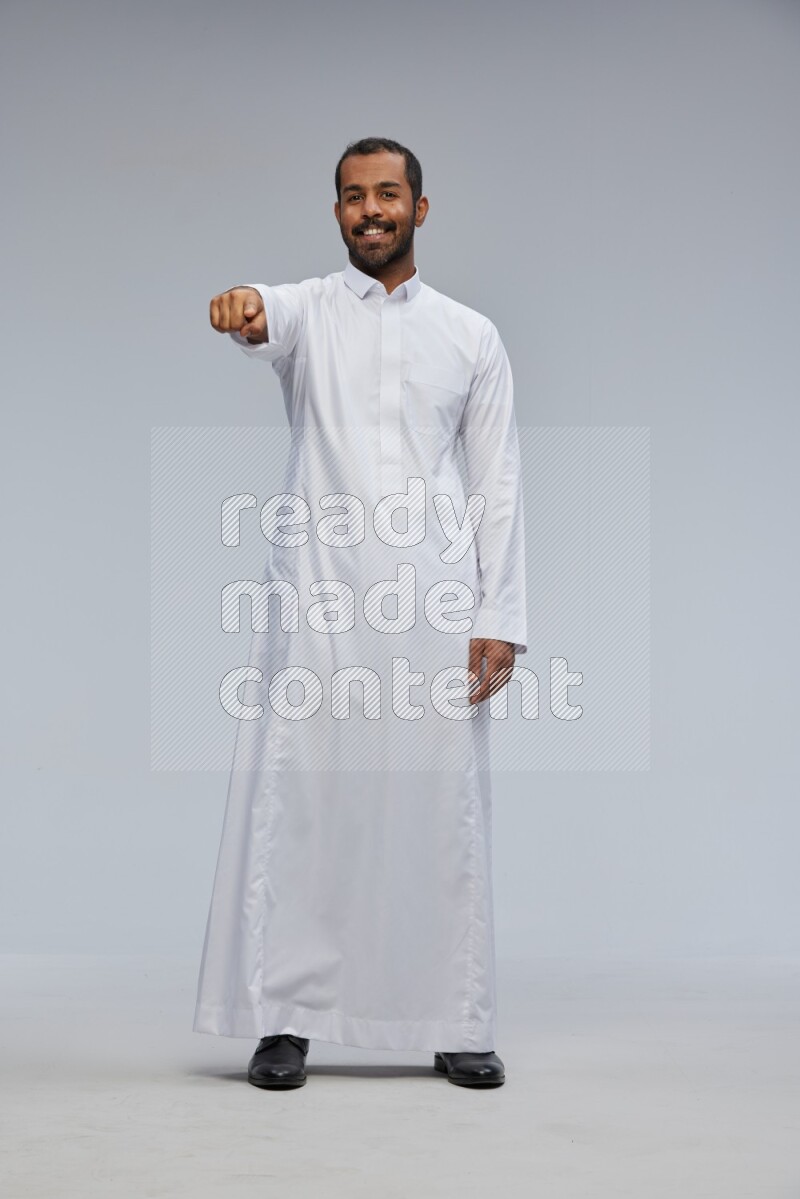 Saudi man Wearing Thob standing interacting with the camera on Gray background