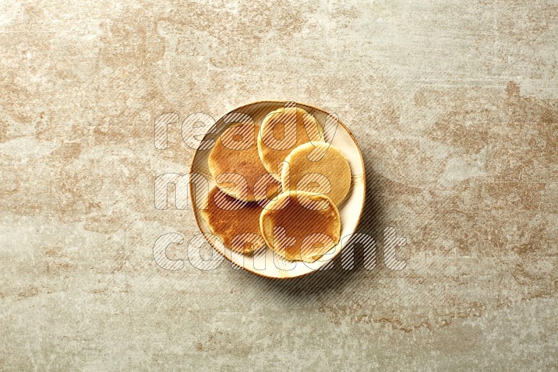 Five stacked plain mini pancakes in an irregular plate on beige background