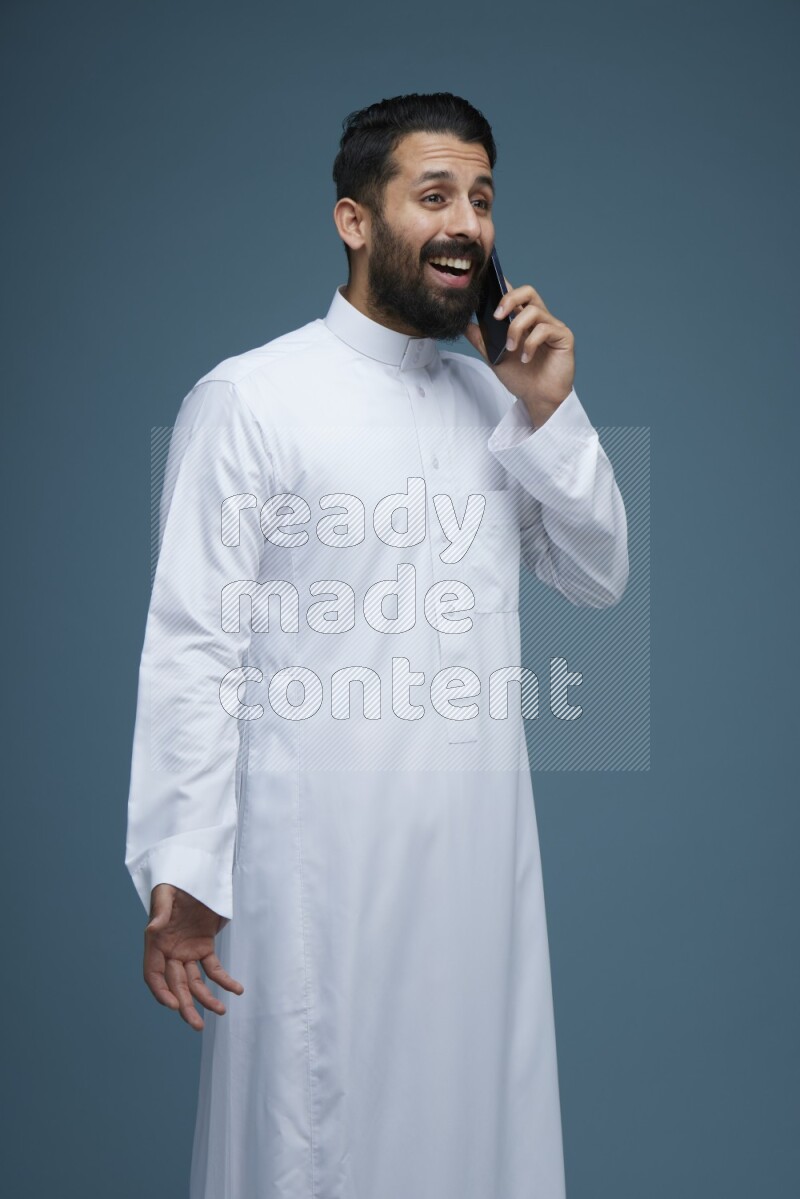 A man having a call on a blue background wearing Saudi Thob