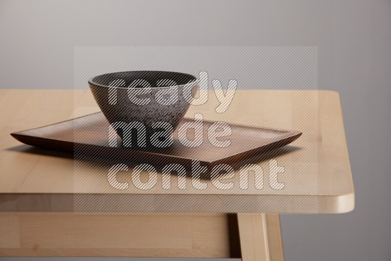 multicolored bowl placed on a rectangular wooden tray on the edge of wooden table