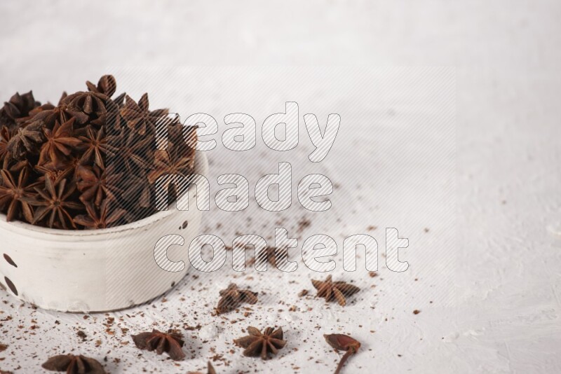 Star Anise in a white bowl and more of it sprinkled on white background