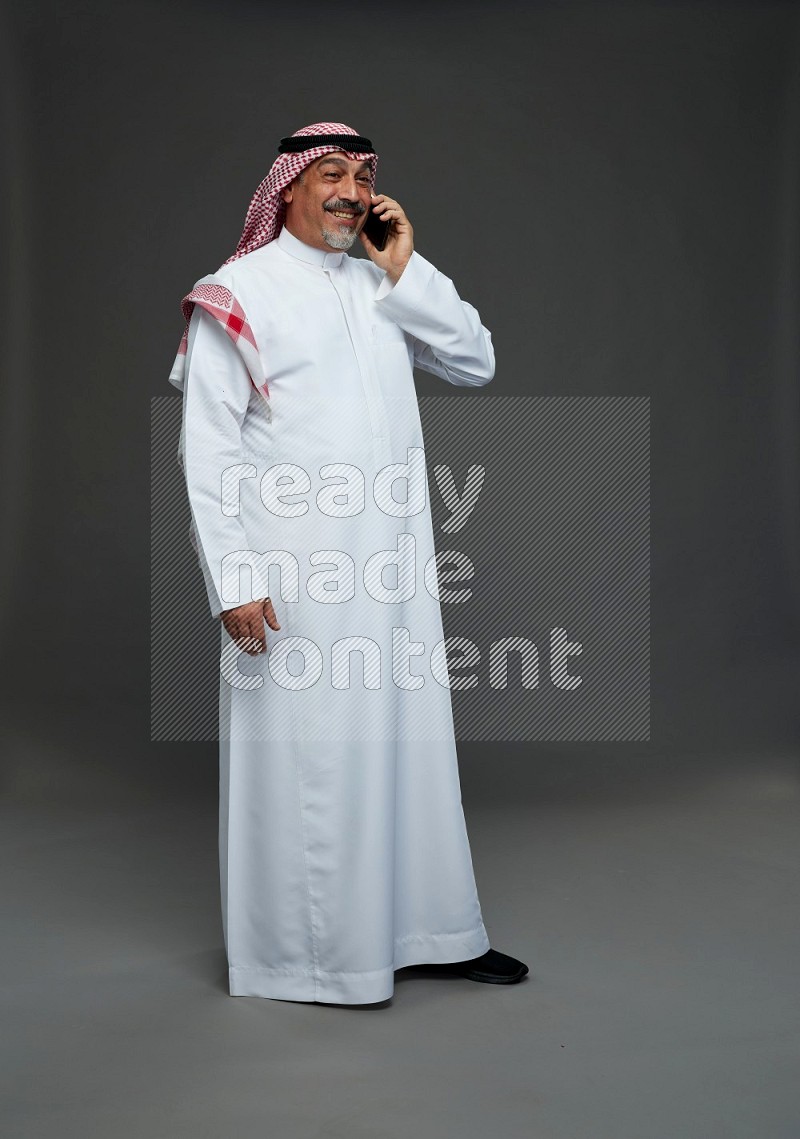 Saudi man with shomag Standing talking on phone on gray background