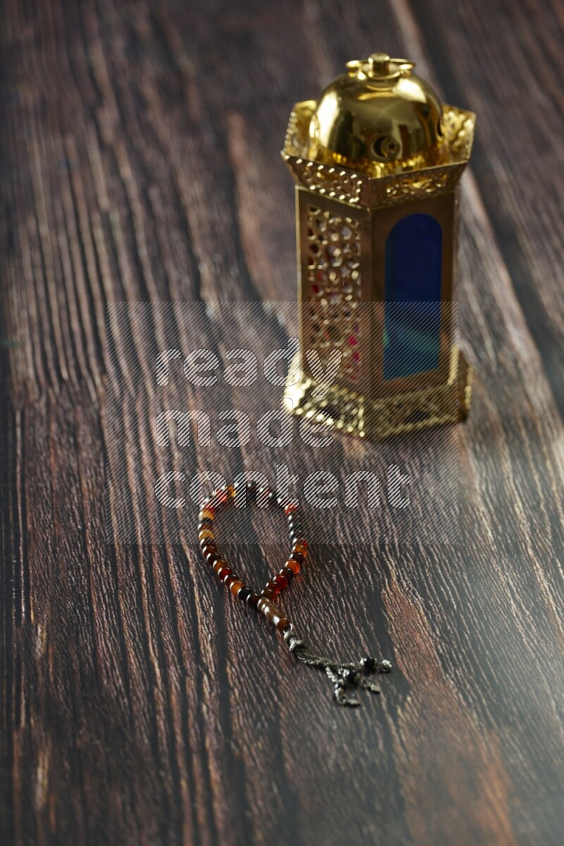 A golden lantern with different drinks, dates, nuts, prayer beads and quran on brown wooden background