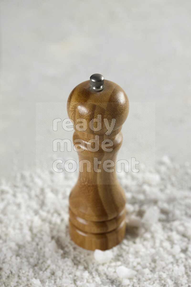 A wooden grinder standing upright and surrounded by coarse white seaa salt on white background
