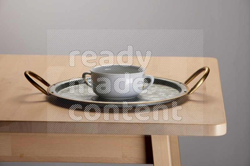 white bowl placed on a rounded stainless steel tray with golden handels on the edge of wooden table