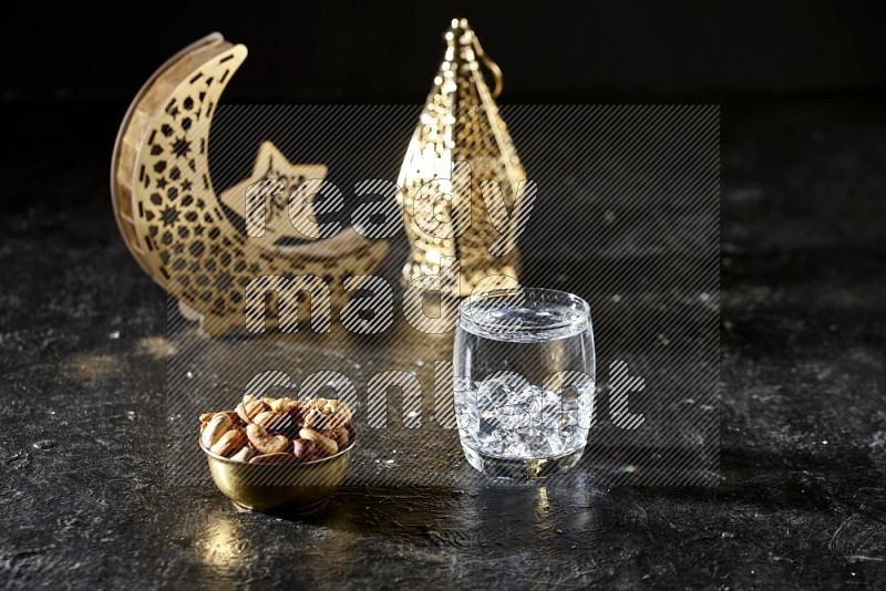 Nuts in a metal bowl with water beside golden lanterns in a dark setup