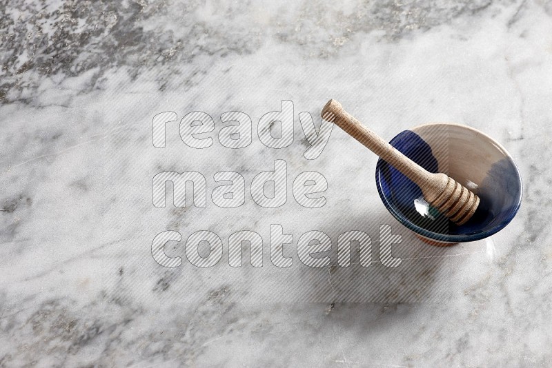 Multicolored Pottery bowl with wooden honey handle in it, on grey marble flooring, 65 degree angle