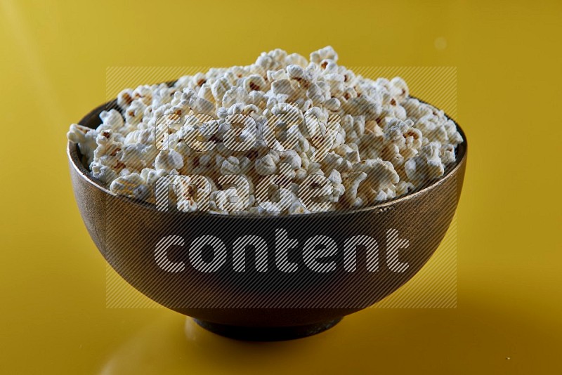 A copper ceramic bowl full of popcorn on a yellow background in different angles