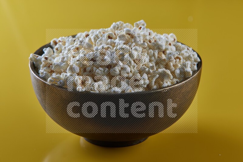 A copper ceramic bowl full of popcorn on a yellow background in different angles