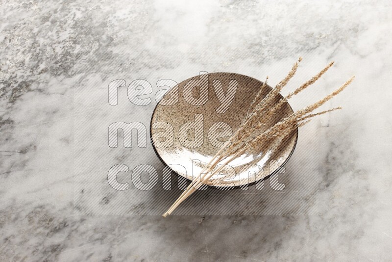 Wheat stalks on multicolored pottery plate on grey marble background