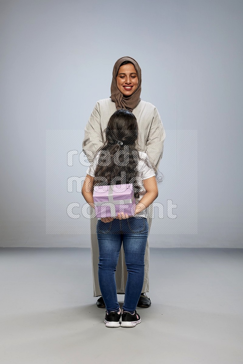 A girl standing hiding a gift behind her back for her mother on gray background