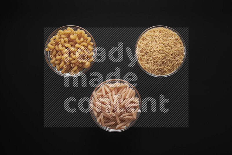 Different pasta types in glass bowls on black background