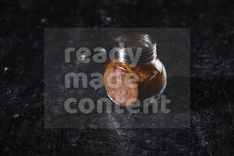 A glass jar full of ground paprika powder on black background