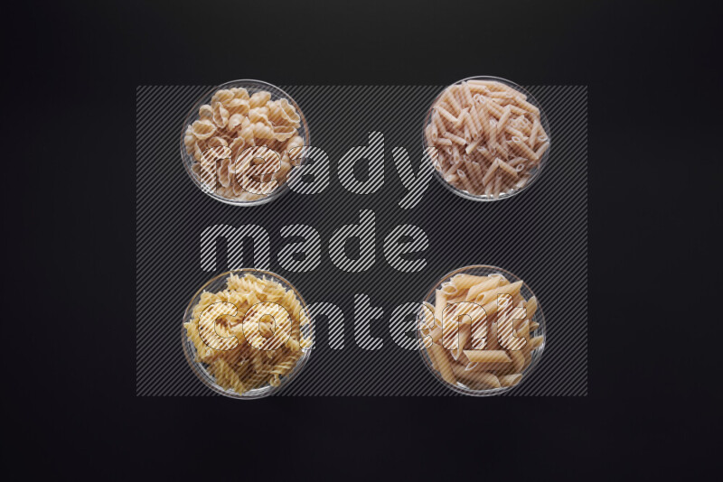 Different pasta types in glass bowls on black background