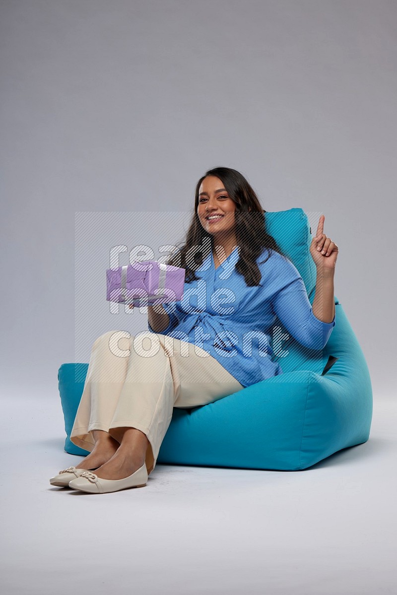 A woman sitting on a blue beanbag and holding a gift