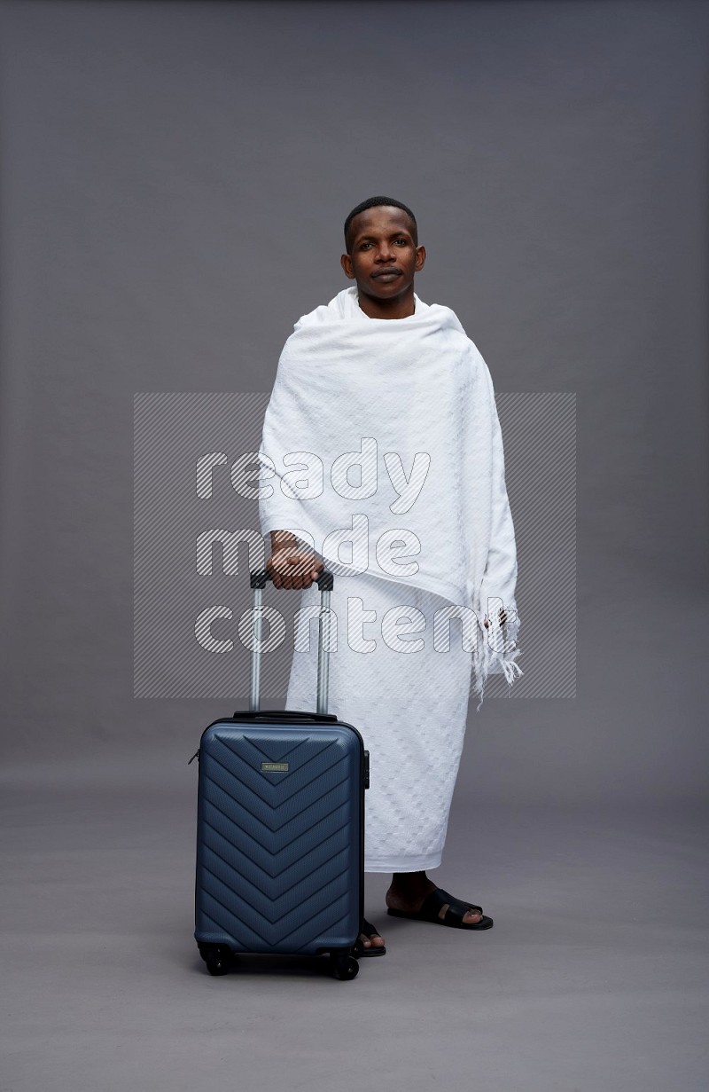 A man wearing Ehram Standing holding traveling bag on gray background