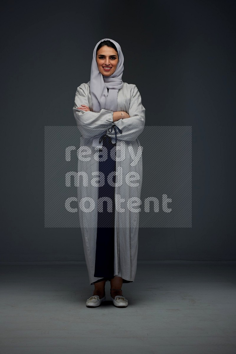 A Saudi woman wearing a light gray Abaya and head scarf standing and making multi poses eye level on a grey background