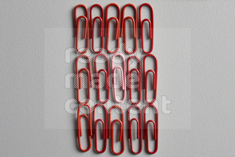 مجموعة من مشابك الورق الحمراء مع مشبك ورق ملون مختلف في المنتصف على خلفية رمادية