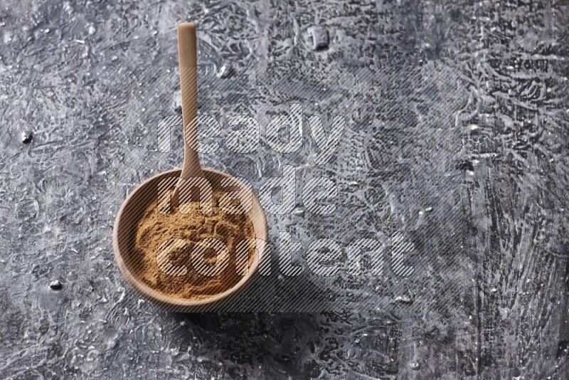 Wooden bowl full of cinnamon powder with a wooden spoon on a textured black background in different angles