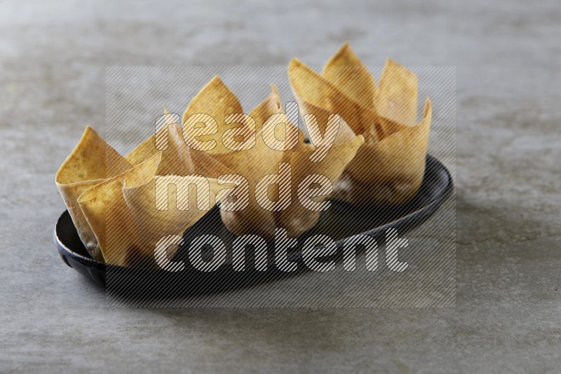 wonton cups on oval black ceramic plate on grey textured counter top