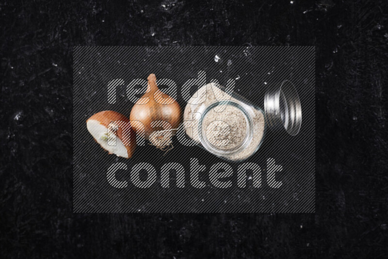 A glass jar full of onion powder on black background