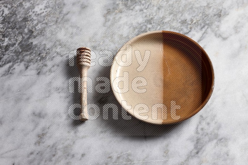 Multicolored Pottery Oven Plate with wooden honey handle on the side with grey marble flooring, 65 degree angle