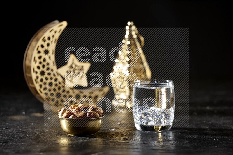 Nuts in a metal bowl with water beside golden lanterns in a dark setup