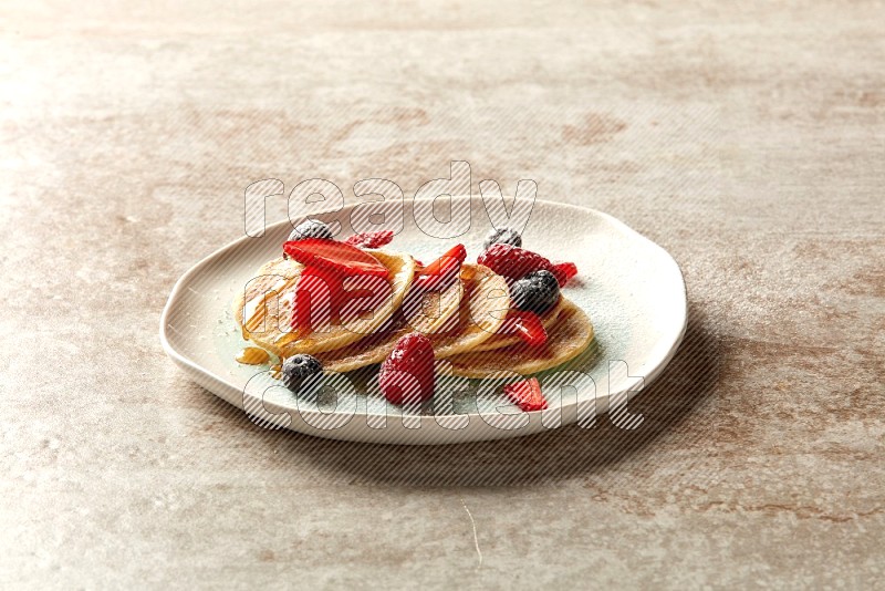 Five stacked mixed berries mini pancakes in a bicolor plate on beige background