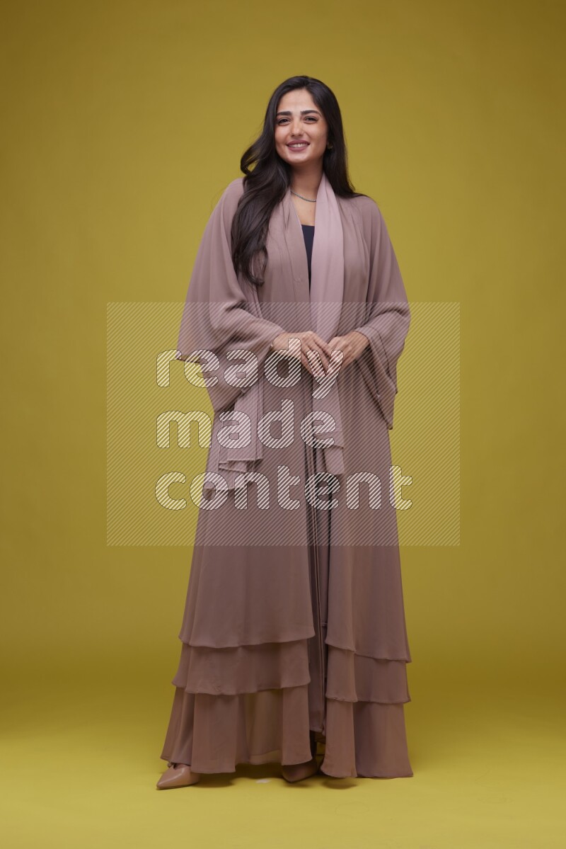 A woman Posing on a Yellow Background wearing Brown Abaya