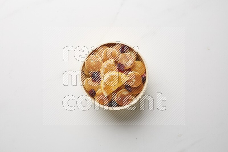 Top-view shot of orange candy cereal pancakes in a round bowl on white background