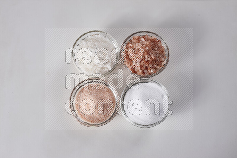 4 glass bowls filled with table salt, coarse sea salt, fine himalayan salt and coarse himalayan salt on white background