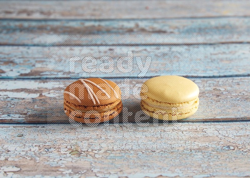 45º Shot of of two assorted Brown Irish Cream, and Yellow Vanilla macarons on light blue background