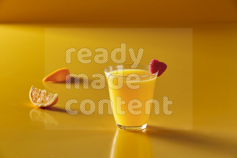 glass of orange juice with berry on yellow background