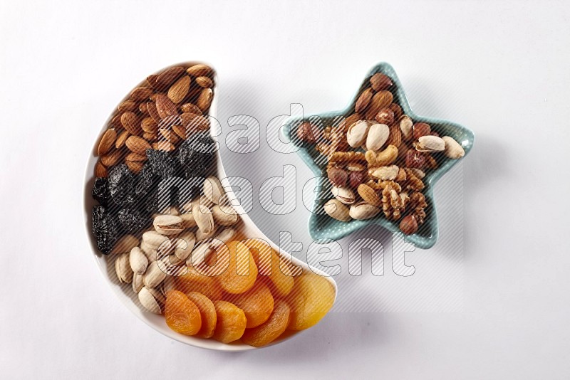 Mixed nuts and dried fruits in a crescent pottery plate and a star shaped plate with Mixed nuts on white background