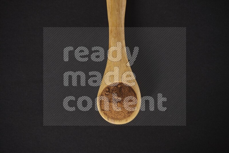 Cinnamon powder in a wooden spoon on a black background