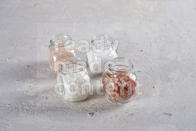 4 glass jars filled with table salt, coarse sea salt, fine himalayan salt and coarse himalayan salt on white background