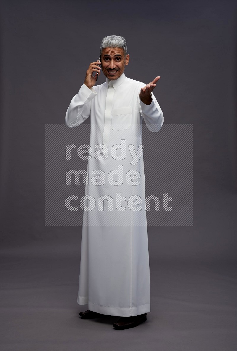 Saudi man wearing thob standing talking on phone on gray background