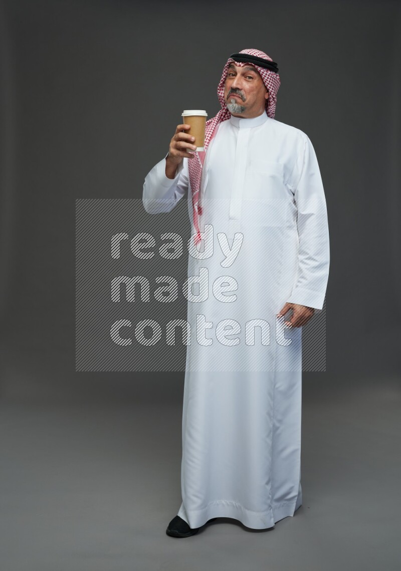 Saudi man with shomag Standing holding paper cup on gray background