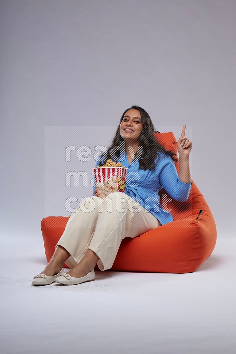 A woman sitting on an orange beanbag and eating popcorn