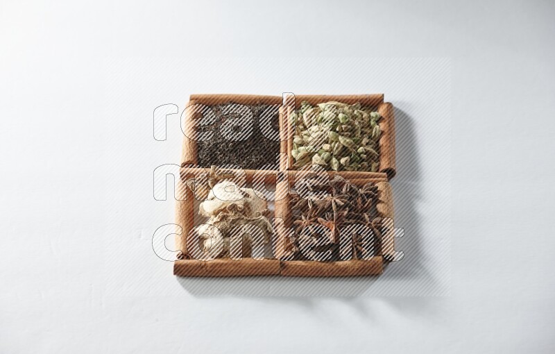 4 مربعات من أعواد القرفة ممتلئة بالشاي والهيل واليانسون والزنجبيل على أرضية بيضاء